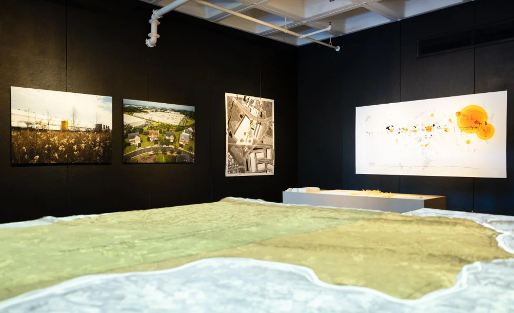 The exhibition installed: aerial photographs and a drawing on black walls, with the topographic model in the foreground.